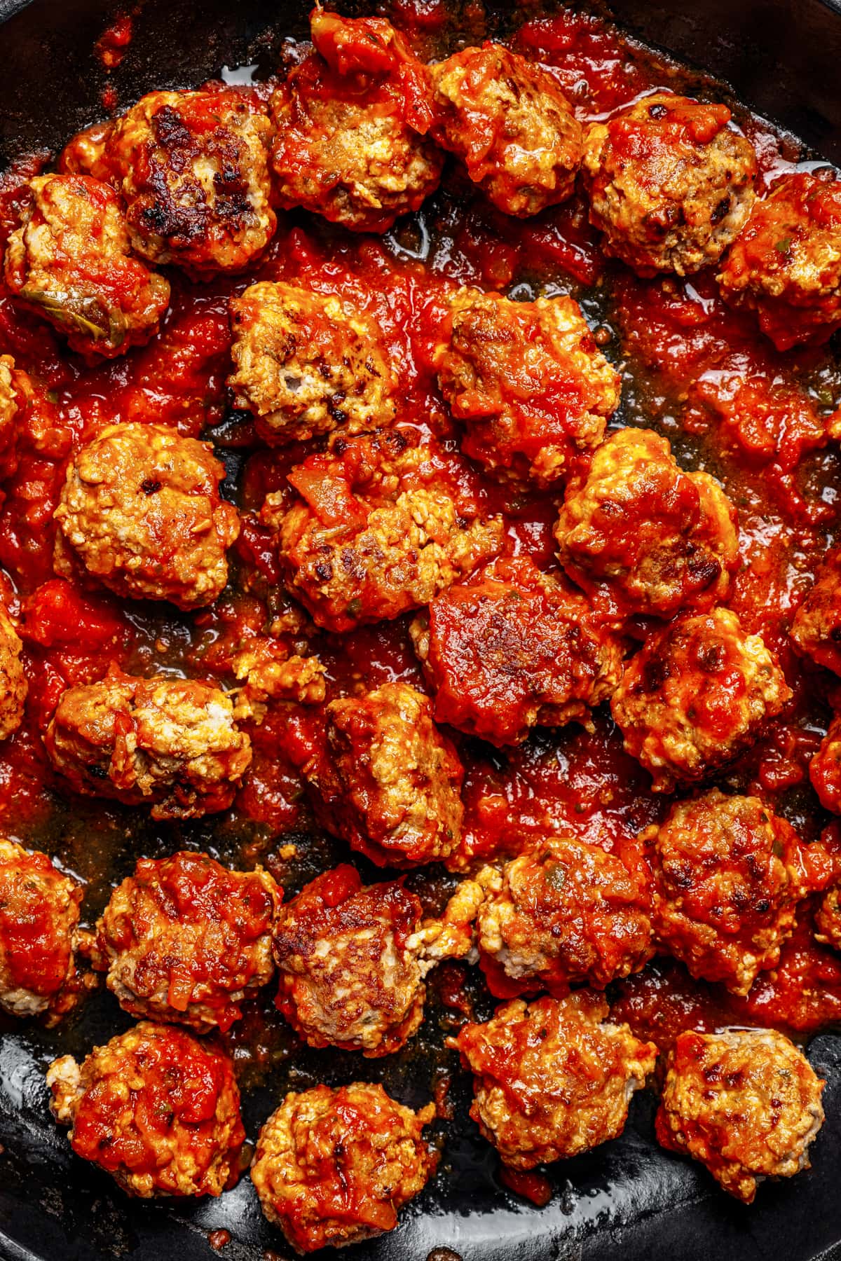 Close up of pork meatballs simmering in marinara sauce in a skillet.