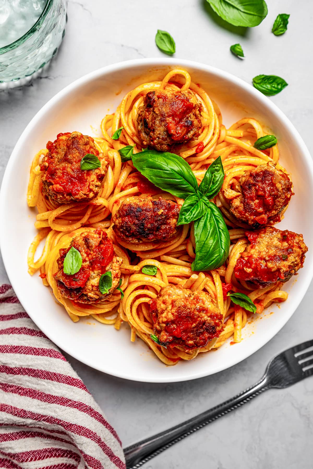 Overhead view of a bowl of spaghetti and pork meatballs garnished with fresh basil leaves.