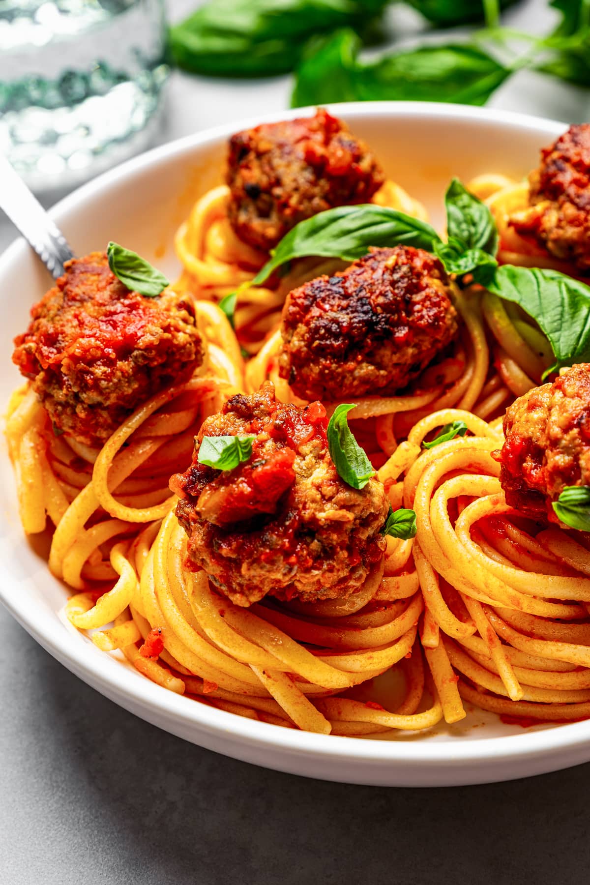 A bowl of spaghetti and pork meatballs garnished with fresh basil leaves.