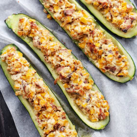Overhead image of four zucchini boats stuffed with cheese, corn, and bacon.