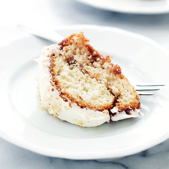 A slice of cinnamon roll coffee cake on a white plate next to a fork.