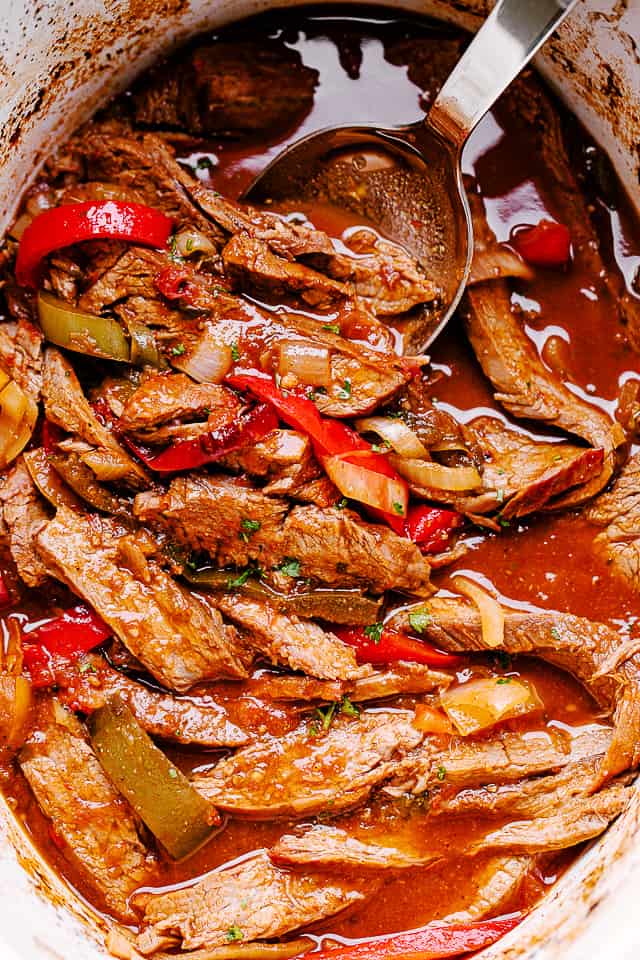 A spoon stirring through cooked slow cooker beef fajitas.