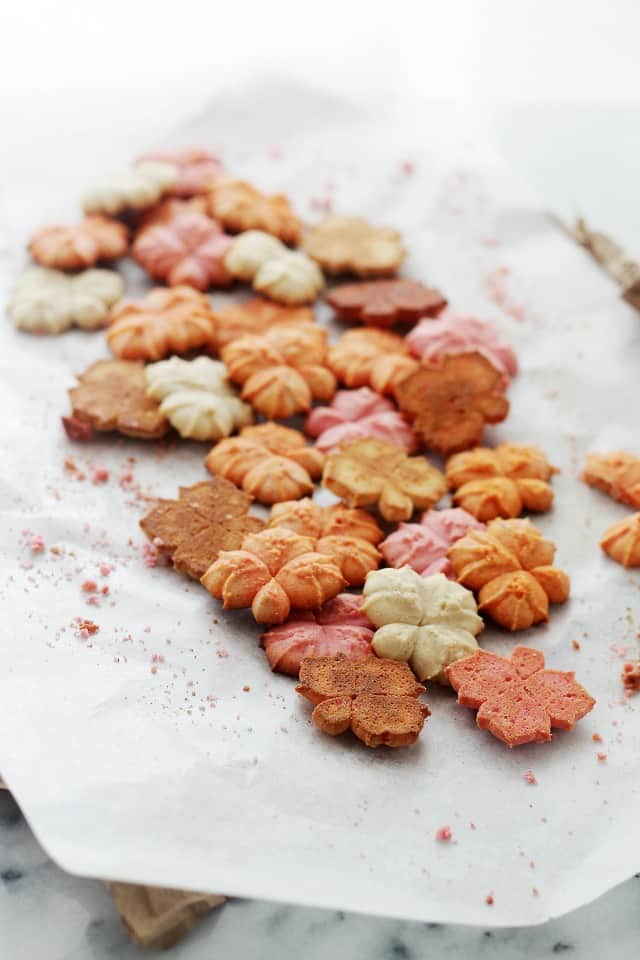 Colorful Spritz Cookies laying on parchment paper with cookie crumbs