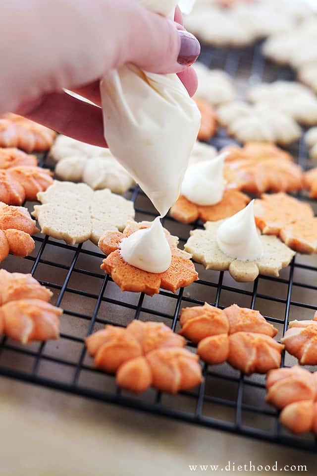 Frosting being squeezed from a bag onto white and orange press cookies