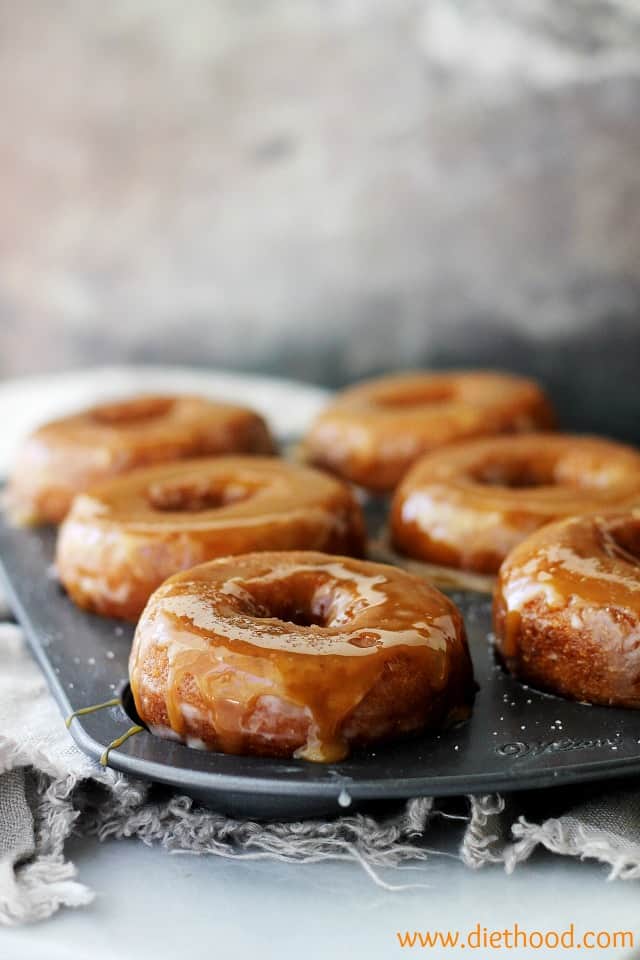 Baked pumpkin donuts glazed with salted caramel sauce in a metal baking pan.