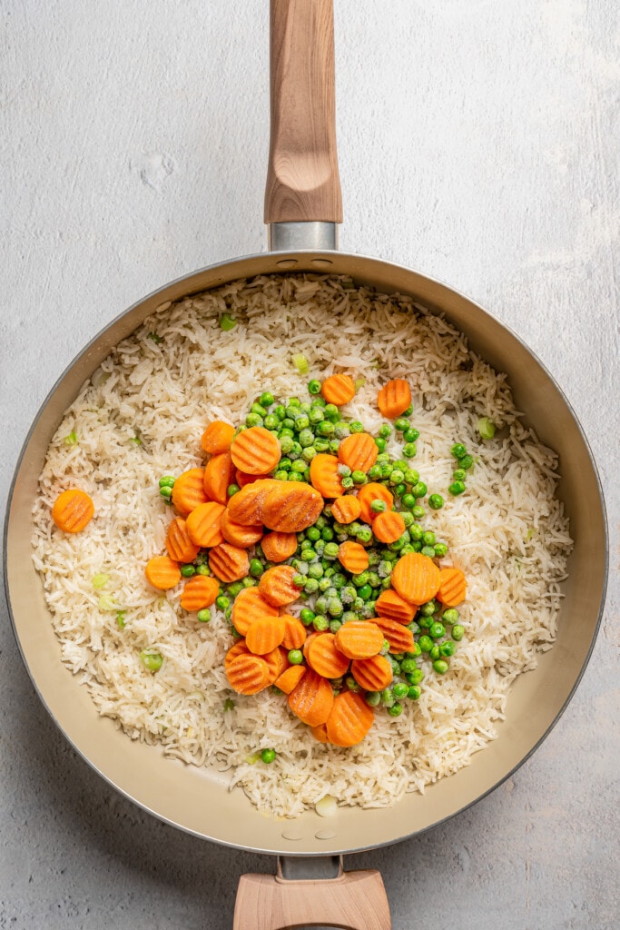 Frozen carrots and peas added to a skillet with fried rice.