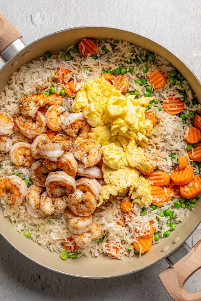 Shrimp and scrambled eggs added to a skillet with fried rice and veggies.