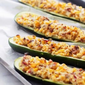 Image of four zucchini boats stuffed with corn, bacon, and cheese.