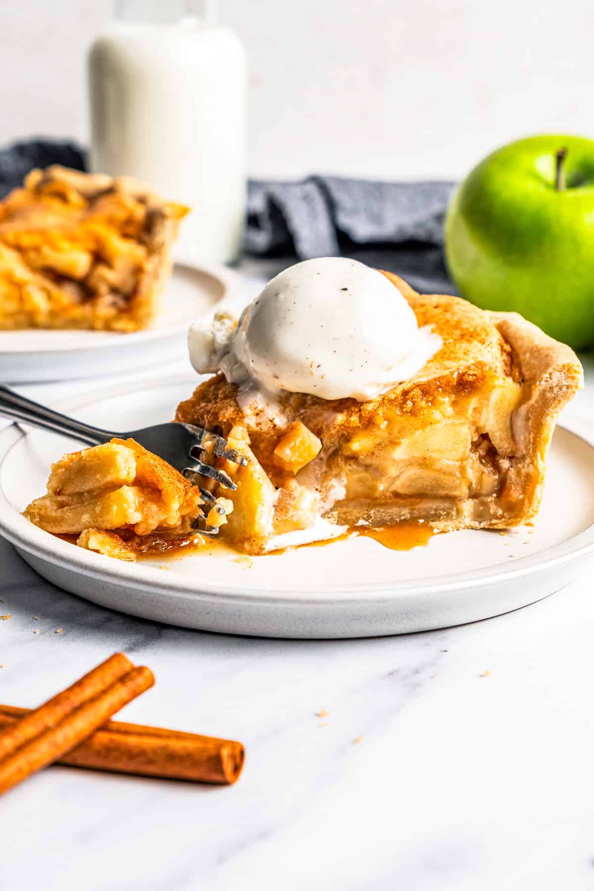 This apple pie cake has juicy caramel apples layered into a buttery crust, baked beneath a soft, sweet cake layer. It's easier than pie! A fork cutting into an apple pie cake served on a plate with a scoop of ice cream on top.