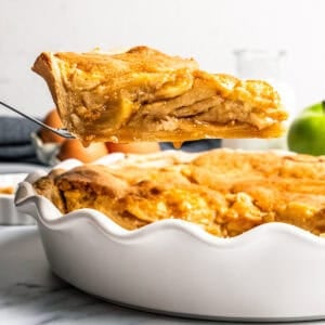 A slice of apple pie cake being lifted from the rest of the cake in a deep dish pie plate.