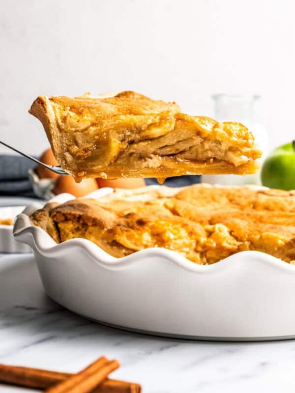 A slice of apple pie cake being lifted from the rest of the cake in a deep dish pie plate.