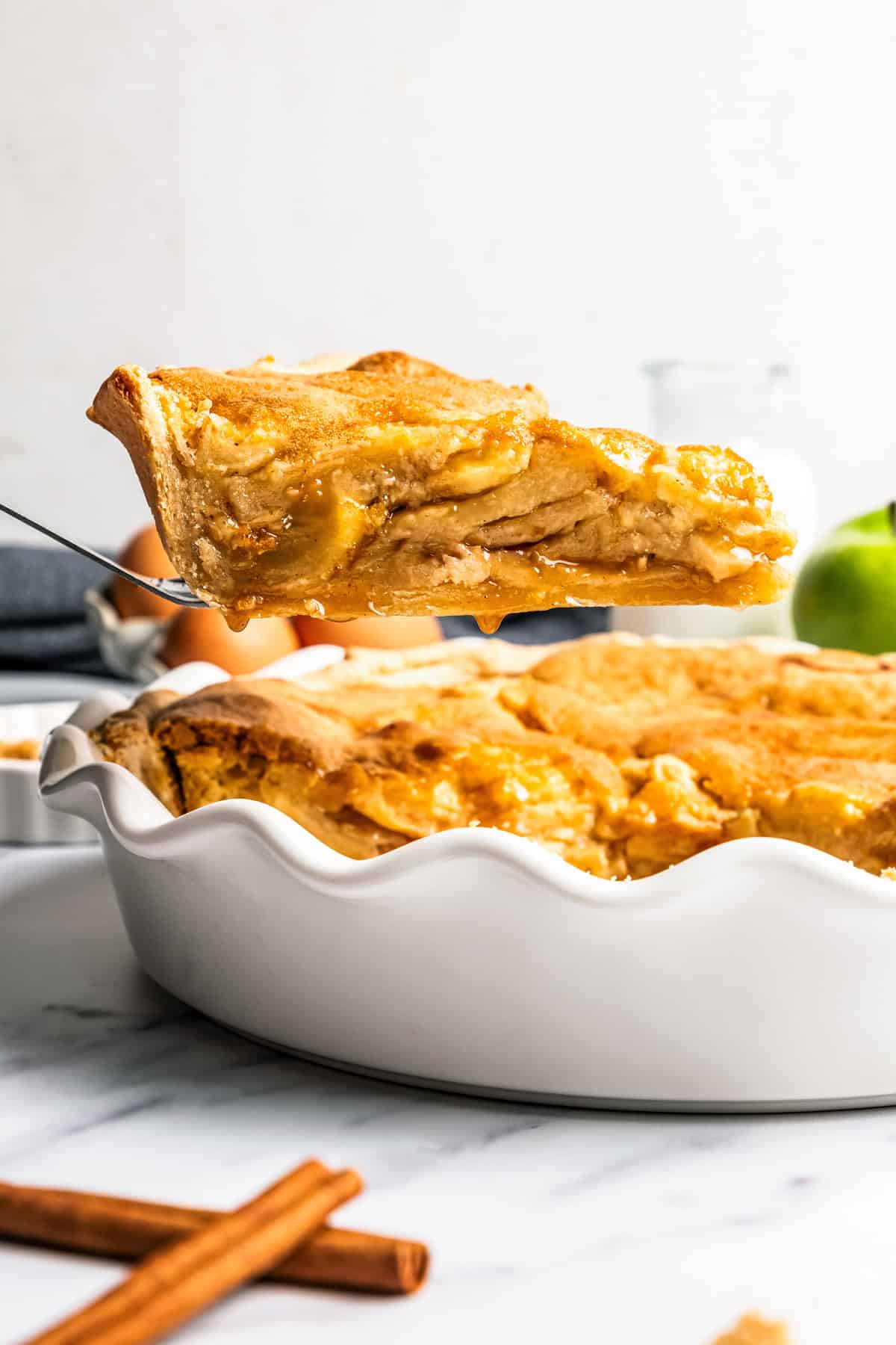 This apple pie cake has juicy caramel apples layered into a buttery crust, baked beneath a soft, sweet cake layer. It's easier than pie! A slice of apple pie cake being lifted from the rest of the cake in a deep dish pie plate.