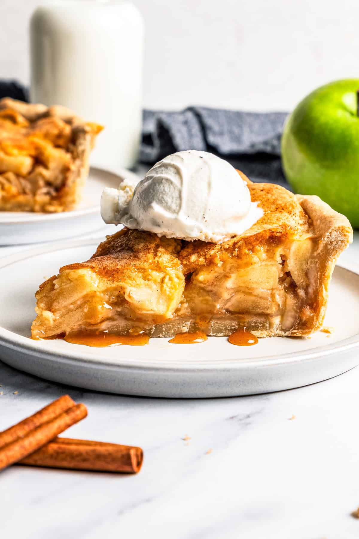 This apple pie cake has juicy caramel apples layered into a buttery crust, baked beneath a soft, sweet cake layer. It's easier than pie! A slice of apple pie cake topped with a scoop of vanilla ice cream on a plate.