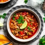 Overhead view of a bowls of chorizo soup garnished with a lime wedge and fresh cilantro, next to a glass of water.