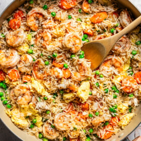 Shrimp fried rice in a skillet with a wooden spoon stirring through it.
