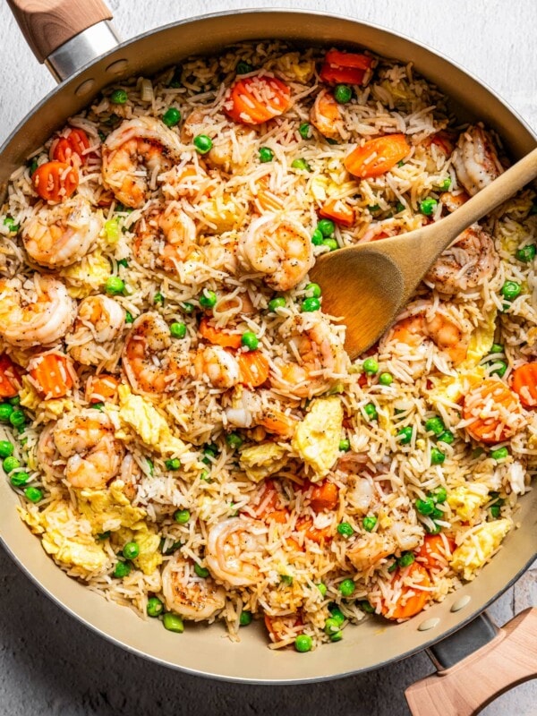 Shrimp fried rice in a skillet with a wooden spoon stirring through it.