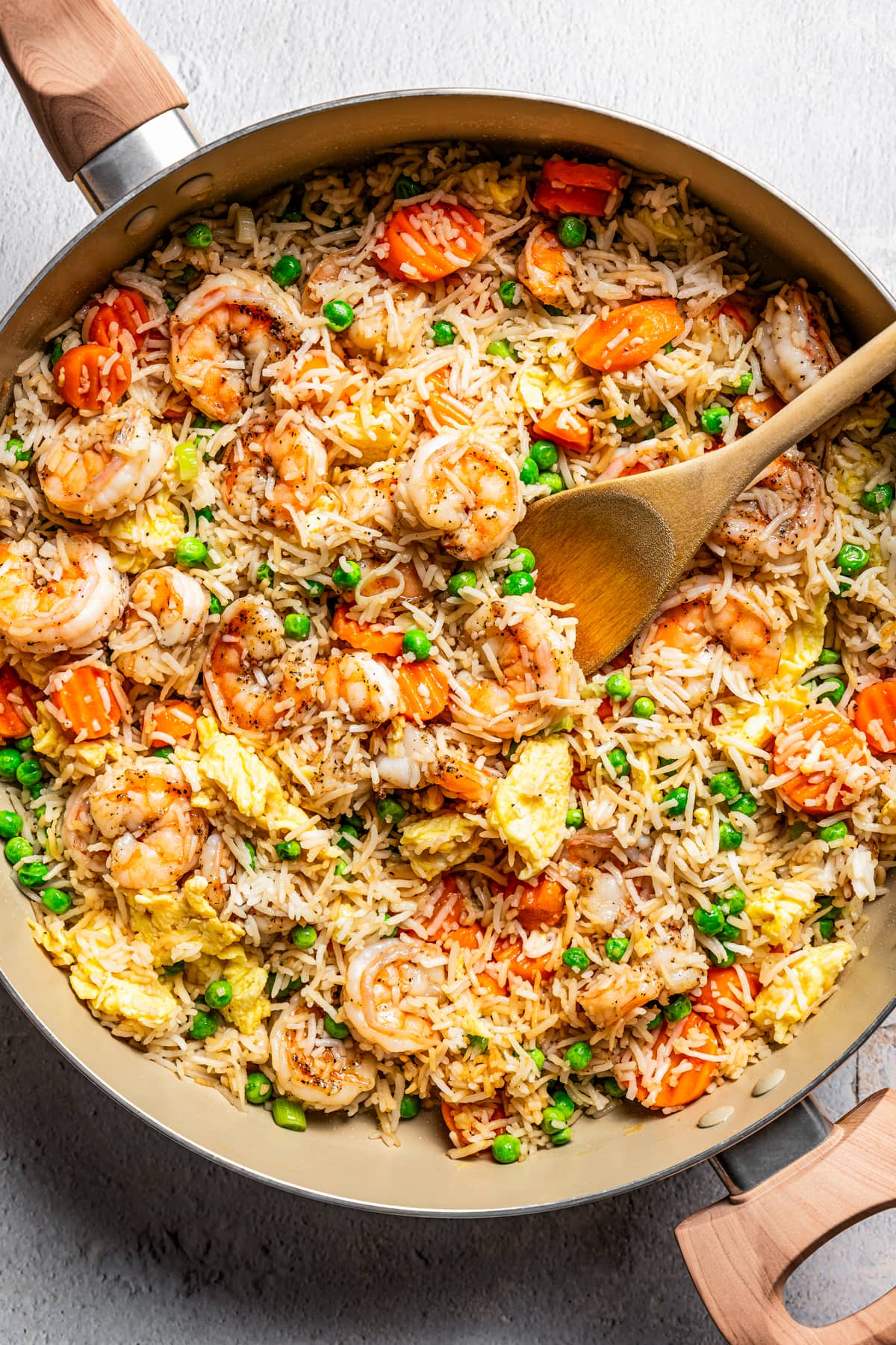 Shrimp fried rice in a skillet with a wooden spoon stirring through it.