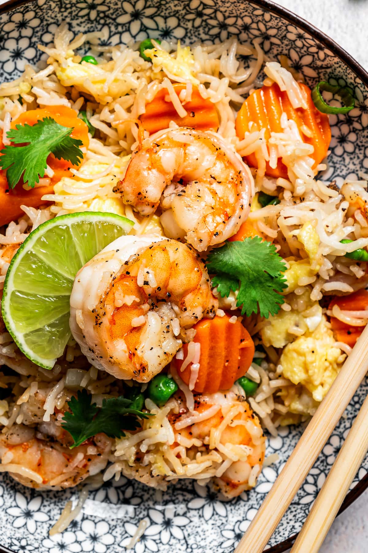 Close-up image of fried rice topped with shrimp, veggies, and a wedge of lime.