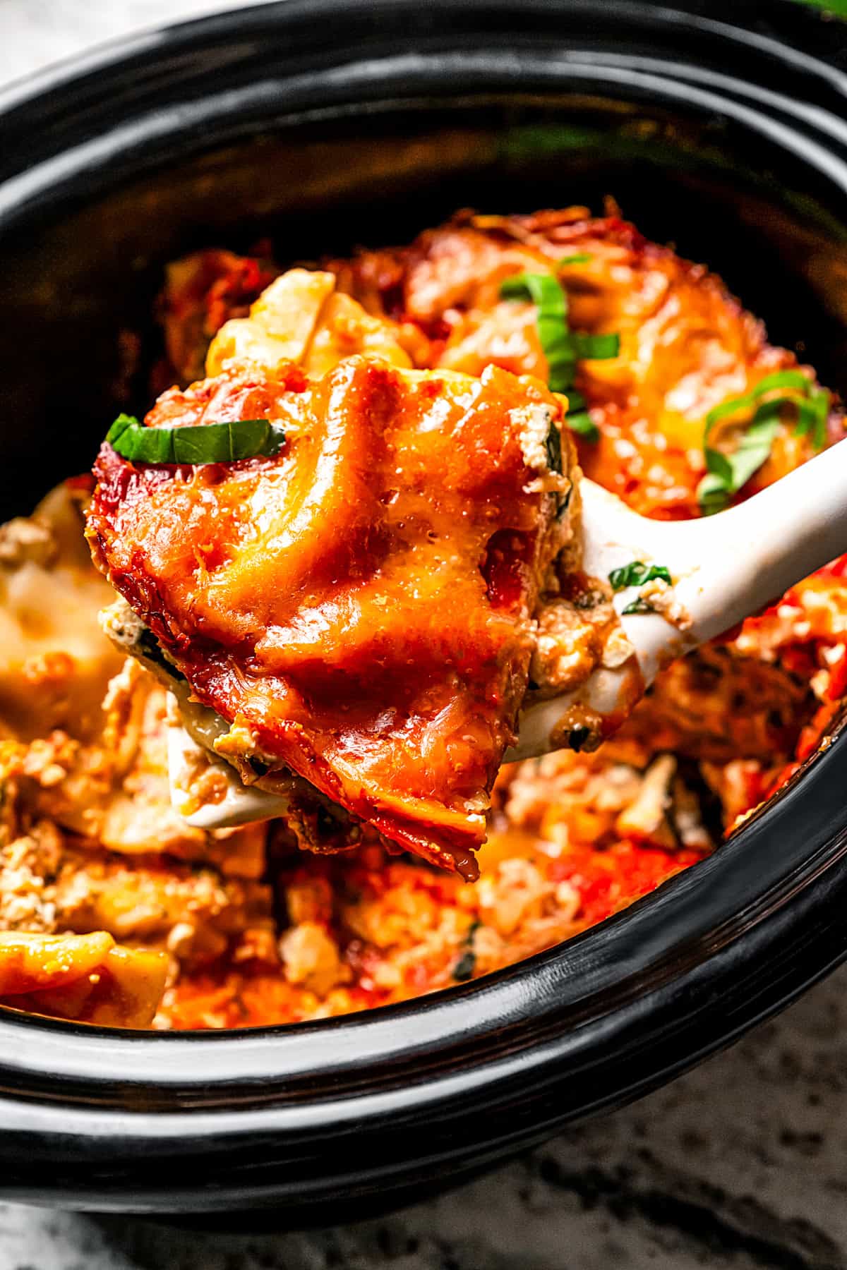 A scoop of crock pot lasagna being served from the crock pot.