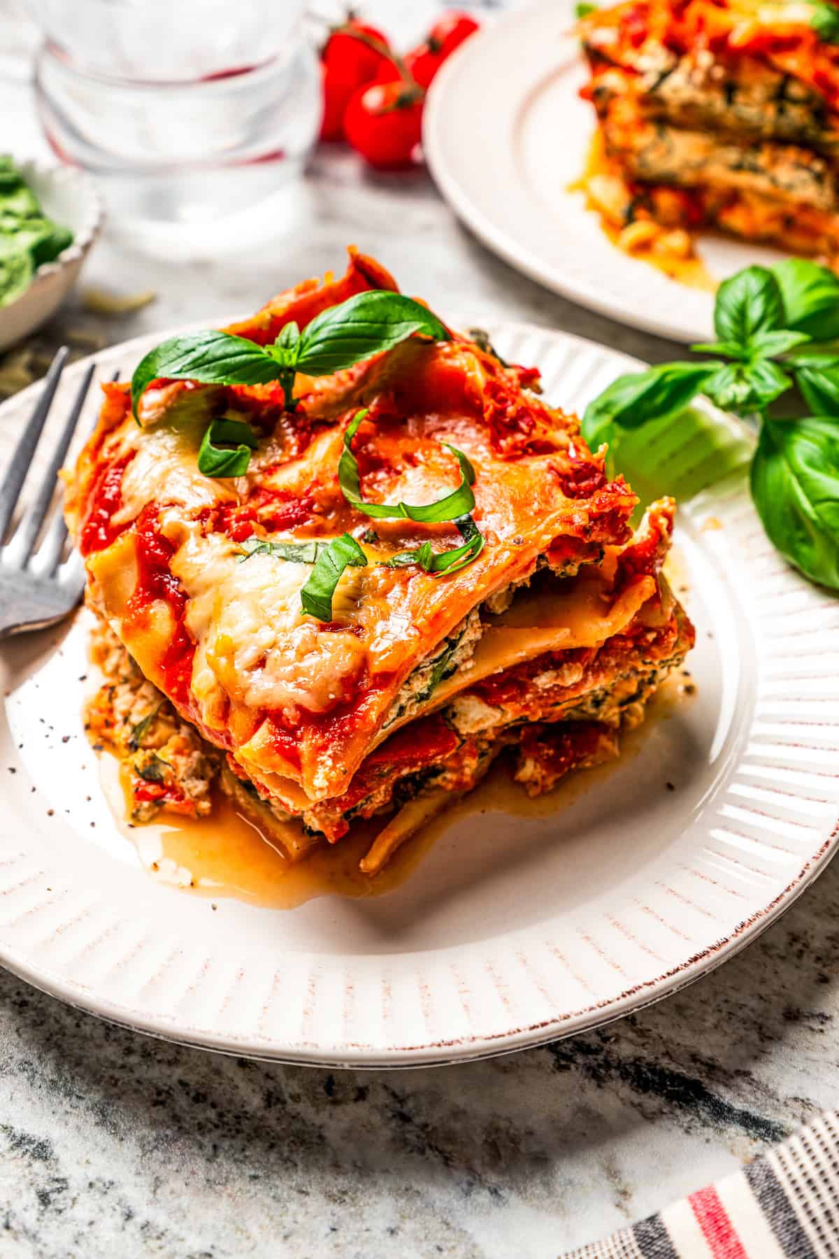 A slice of spinach lasagna served on a dinner plate next to a fork.