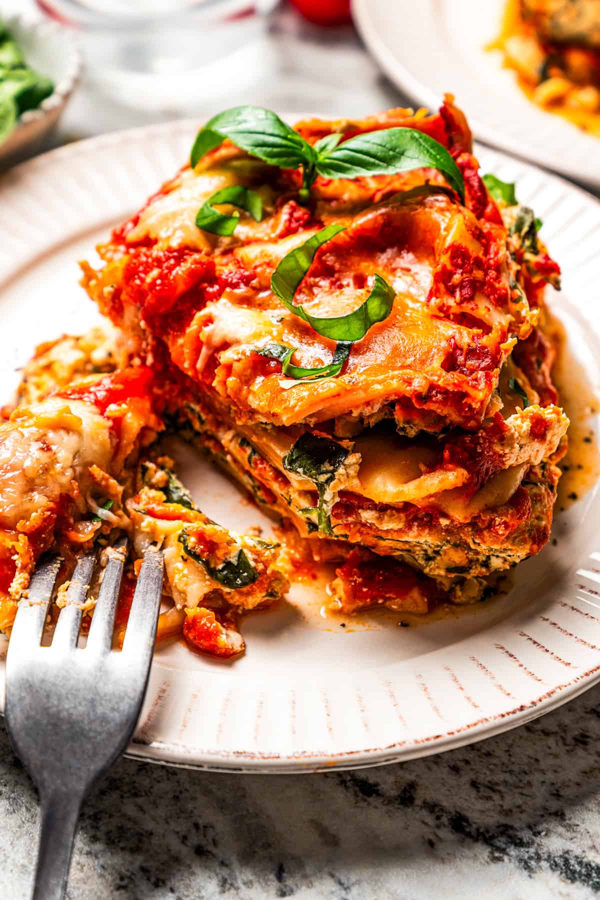 A fork resting next to a half-eaten slice of spinach lasagna on a white plate.