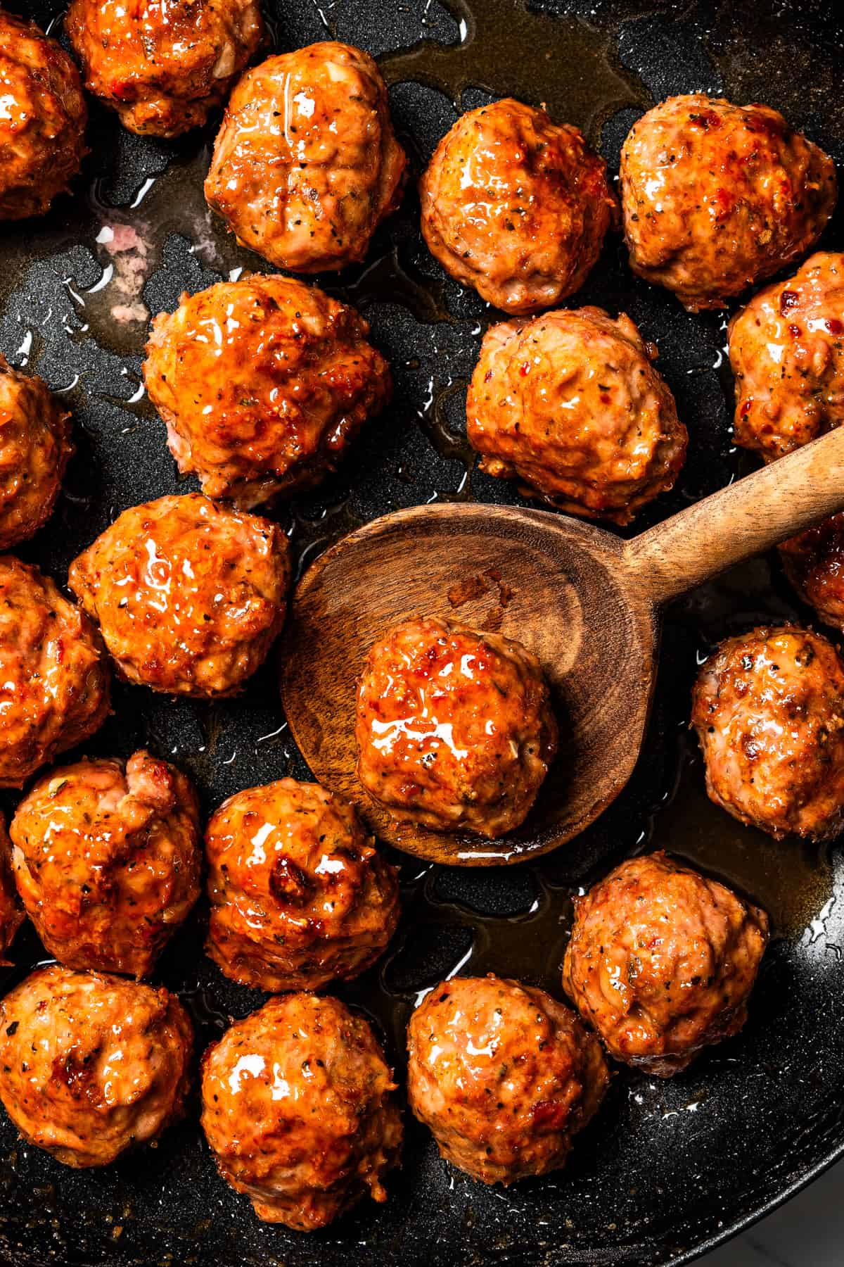 Close-up of a wooden spoon holding a meatball with more glazed turkey meatballs around it.