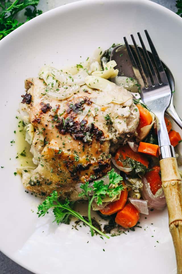 Baked Chicken served on a dinner plate with cooked artichokes, carrots, onions, and baby spinach.