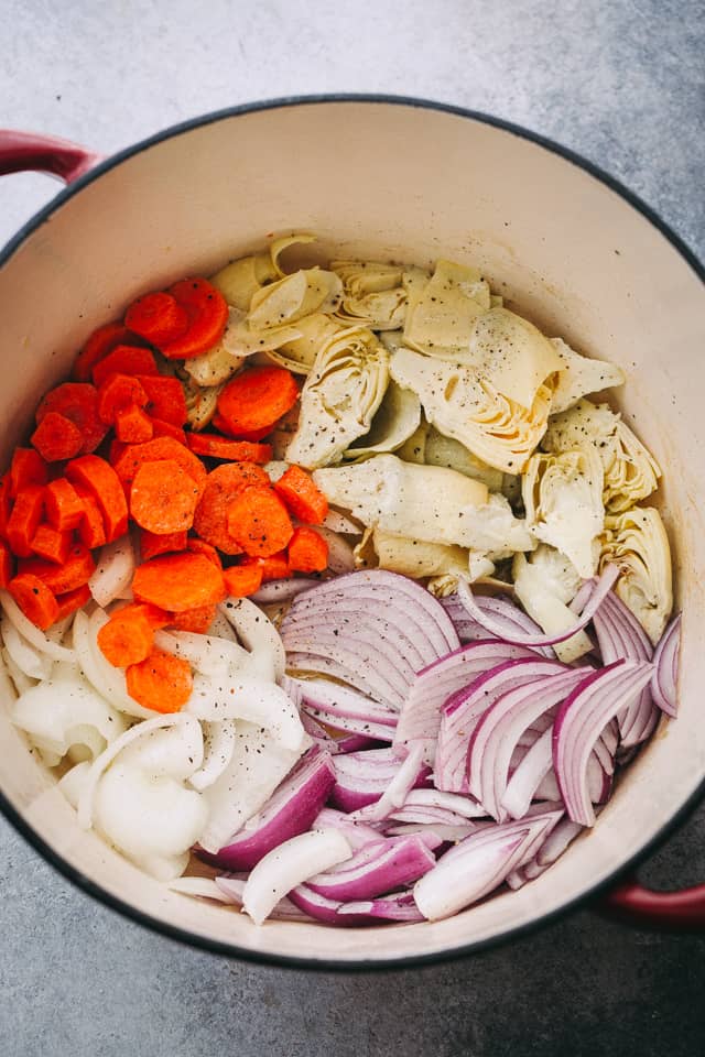 Chopped carrots, artichokes, and onions in a cooking pot.