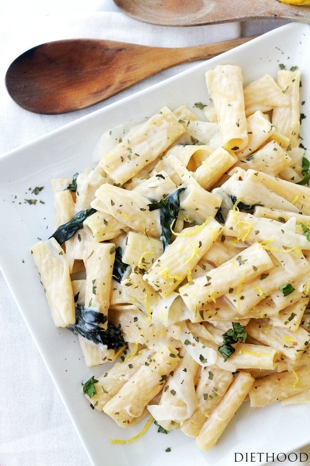 A white plate next to a spoon is filled with creamy pasta topped with herbs