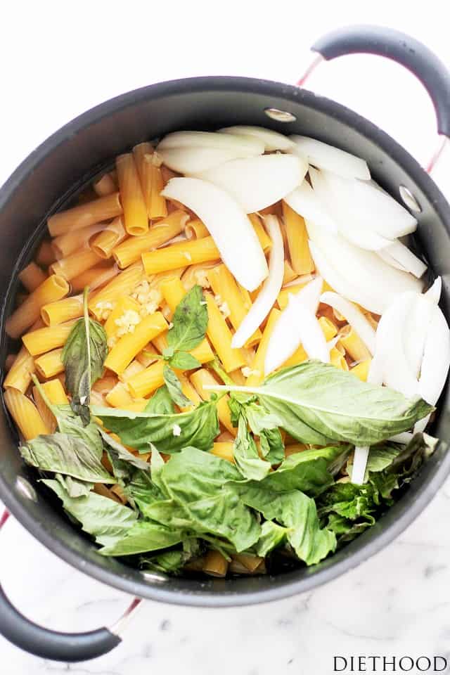 A dark pot filled with pasta and fresh onions and herbs