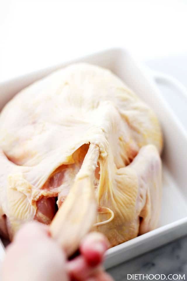 Using a wooden spoon and separating the skin of a whole raw chicken.