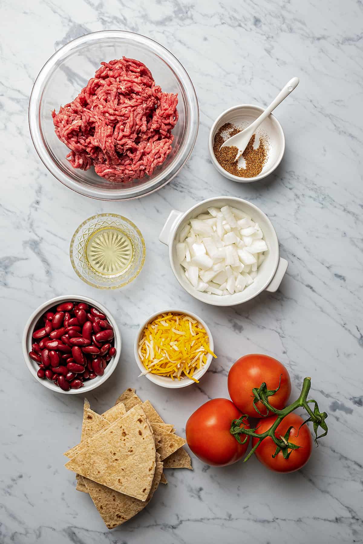 From top: Ground beef, seasonings, olive oil, onion, kidney beans, shredded cheese, tortilla pieces, tomatoes.