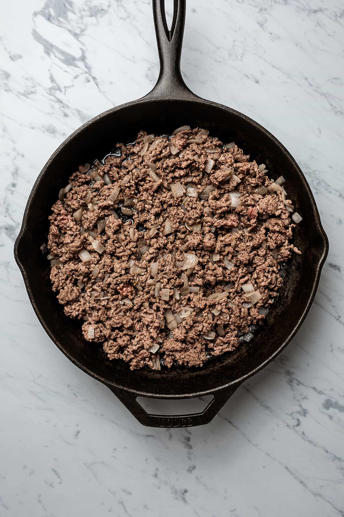 Browned ground beef in a skillet with onions.