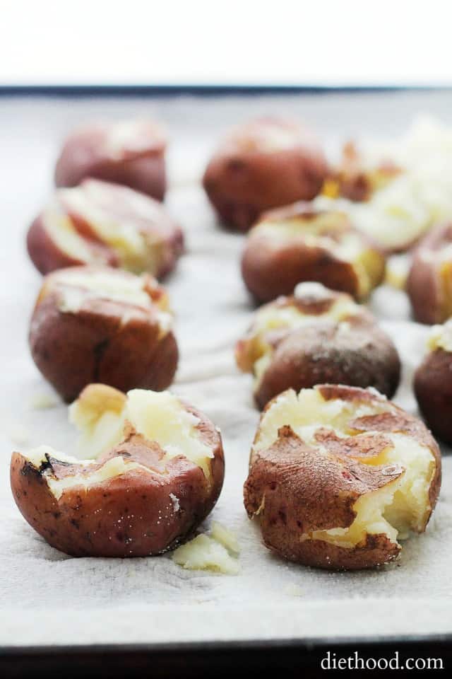 Smashed boiled potatoes in rows on a lined baking sheet.