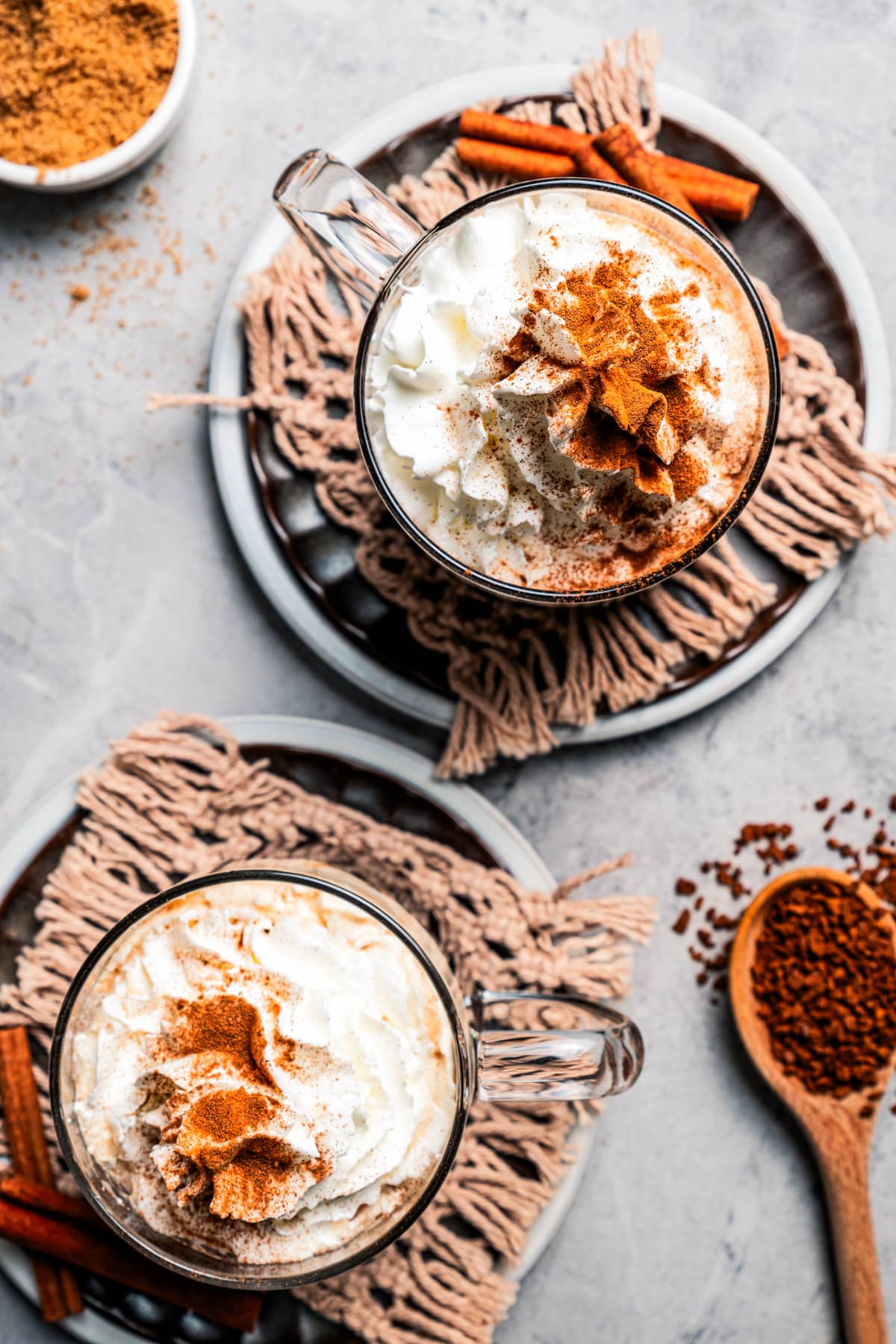 Overhead view of two cinnamon dolce lattes in mugs garnished with whipped cream and dusted with cinnamon.
