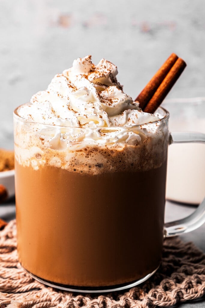 A cinnamon dolce latte in a glass mug garnished with whipped cream and a cinnamon stick, and dusted with ground cinnamon.