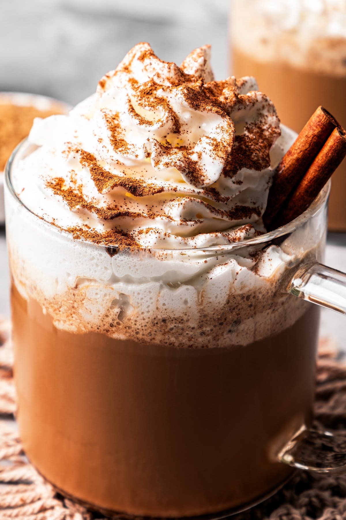 A cinnamon dolce latte in a glass mug garnished with whipped cream and a cinnamon stick, and dusted with ground cinnamon.