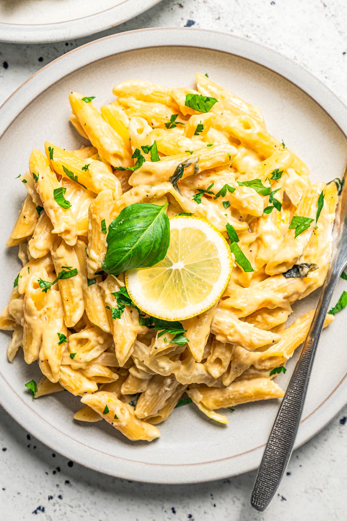 Bowl of lemon pasta recipe with a lemon slice and fresh parsley and basil on top.