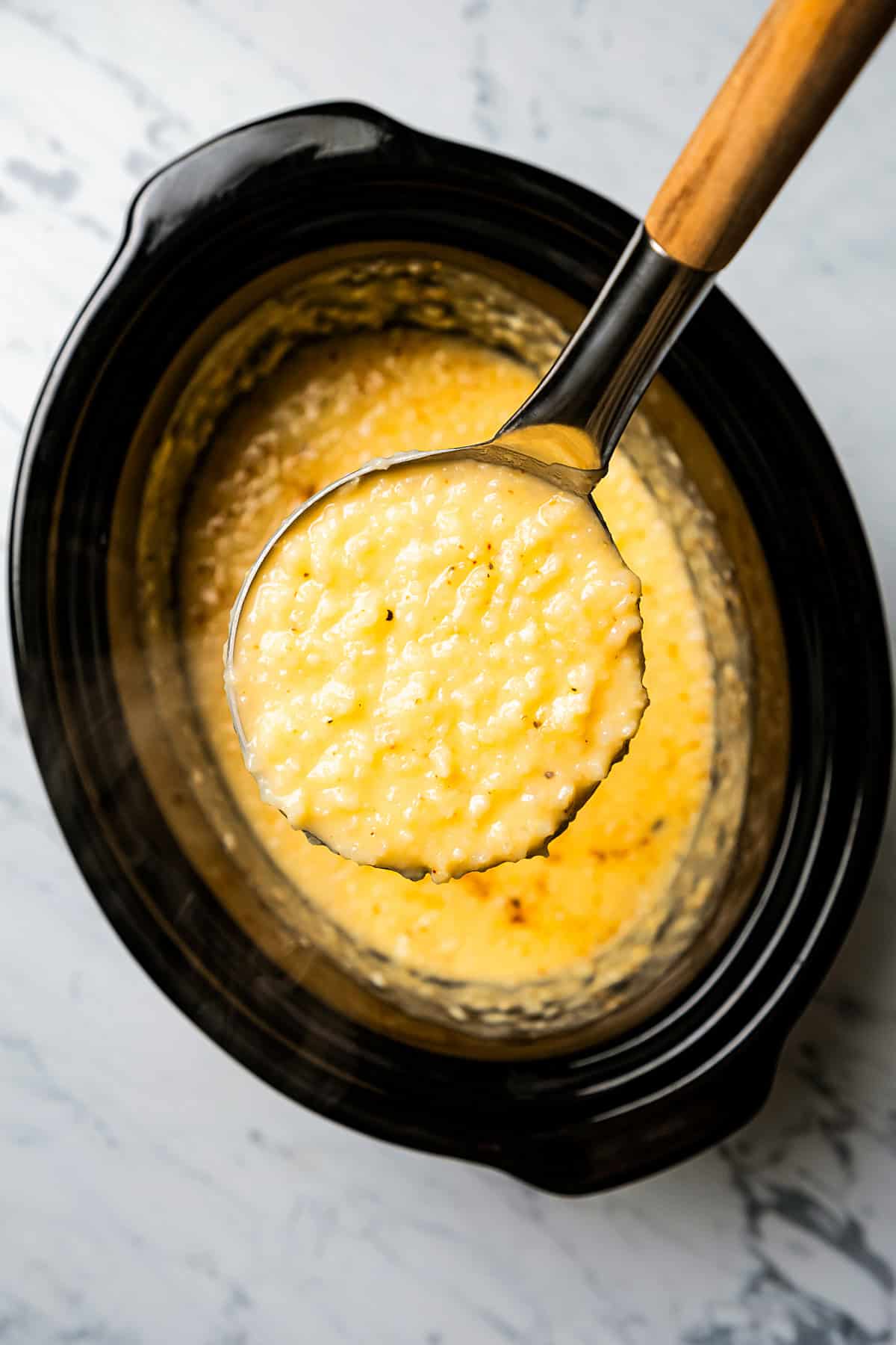 A ladleful of lemon rice soup was held above the crock pot.