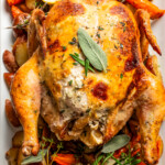 Overhead image of roast chicken on a serving platter over roasted veggies.