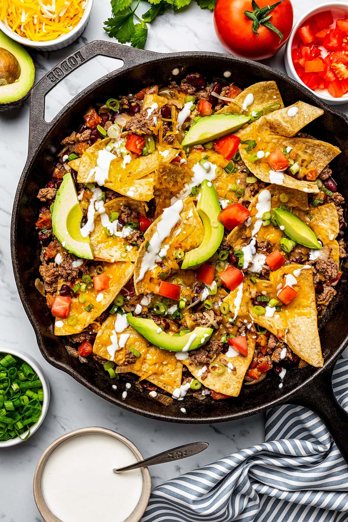 A skillet of cooked ground beef, tomatoes, cheese, and beans, and topped with tortilla chips.