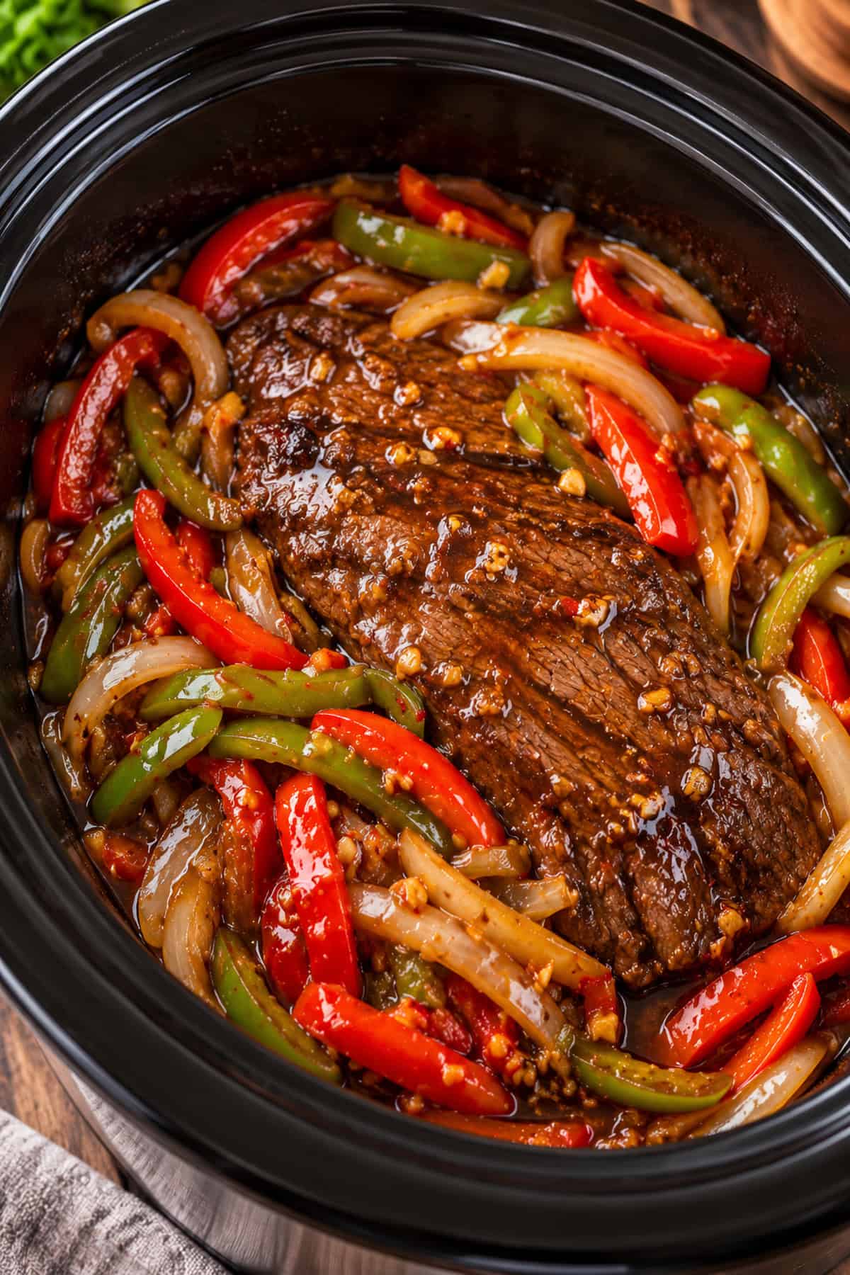 Whole flank steak with bell peppers and onions cooking in the slow cooker.