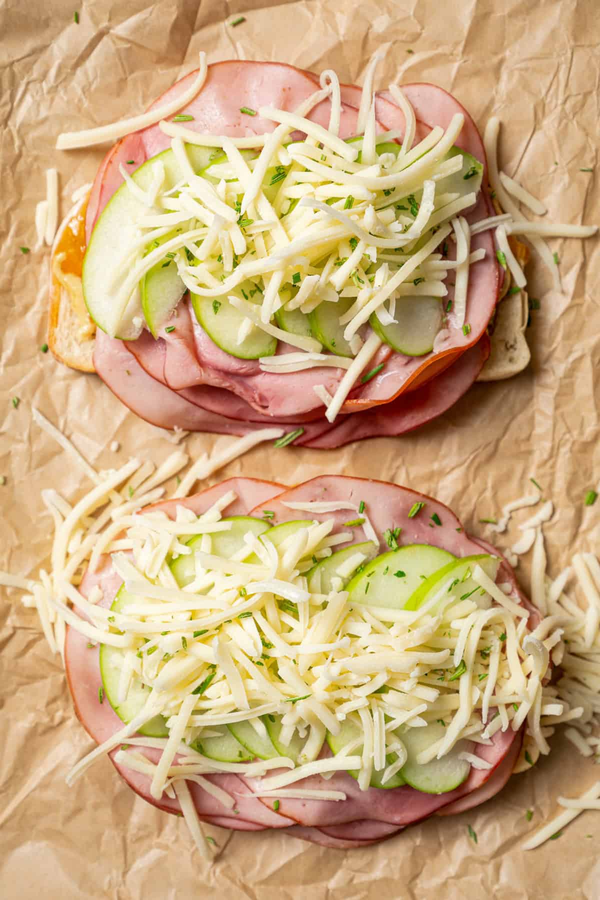 Overhead view of two partially assembled apple grilled cheese sandwiches on a piece of parchment paper.