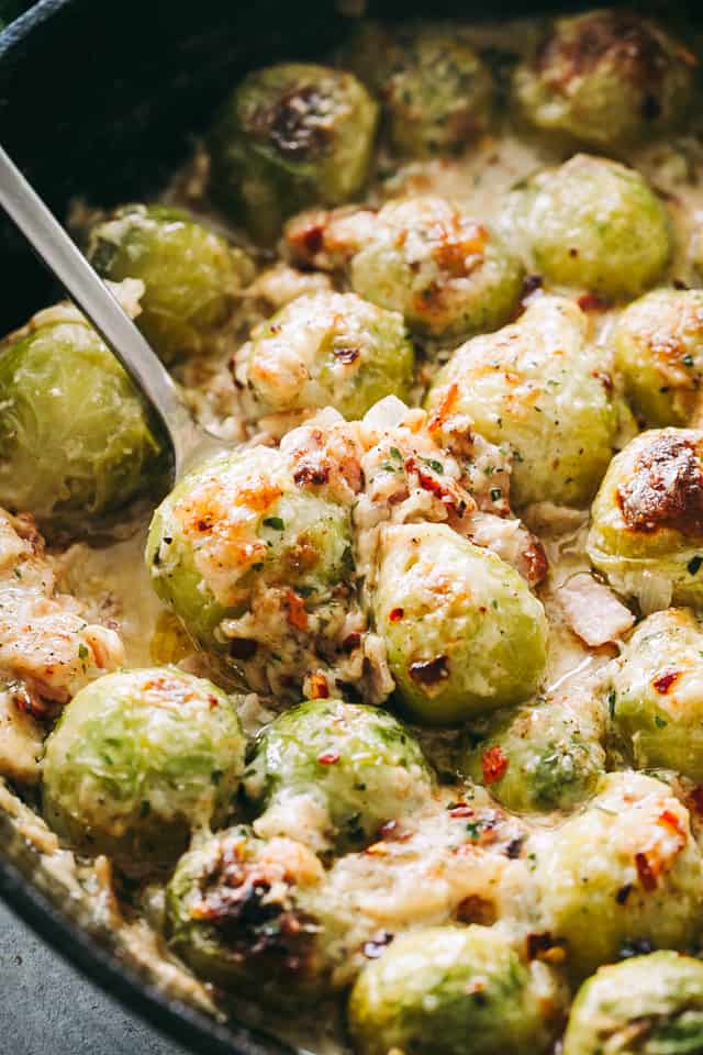 A spoon is used to serve cheesy roasted Brussels sprouts with bacon from a skillet.