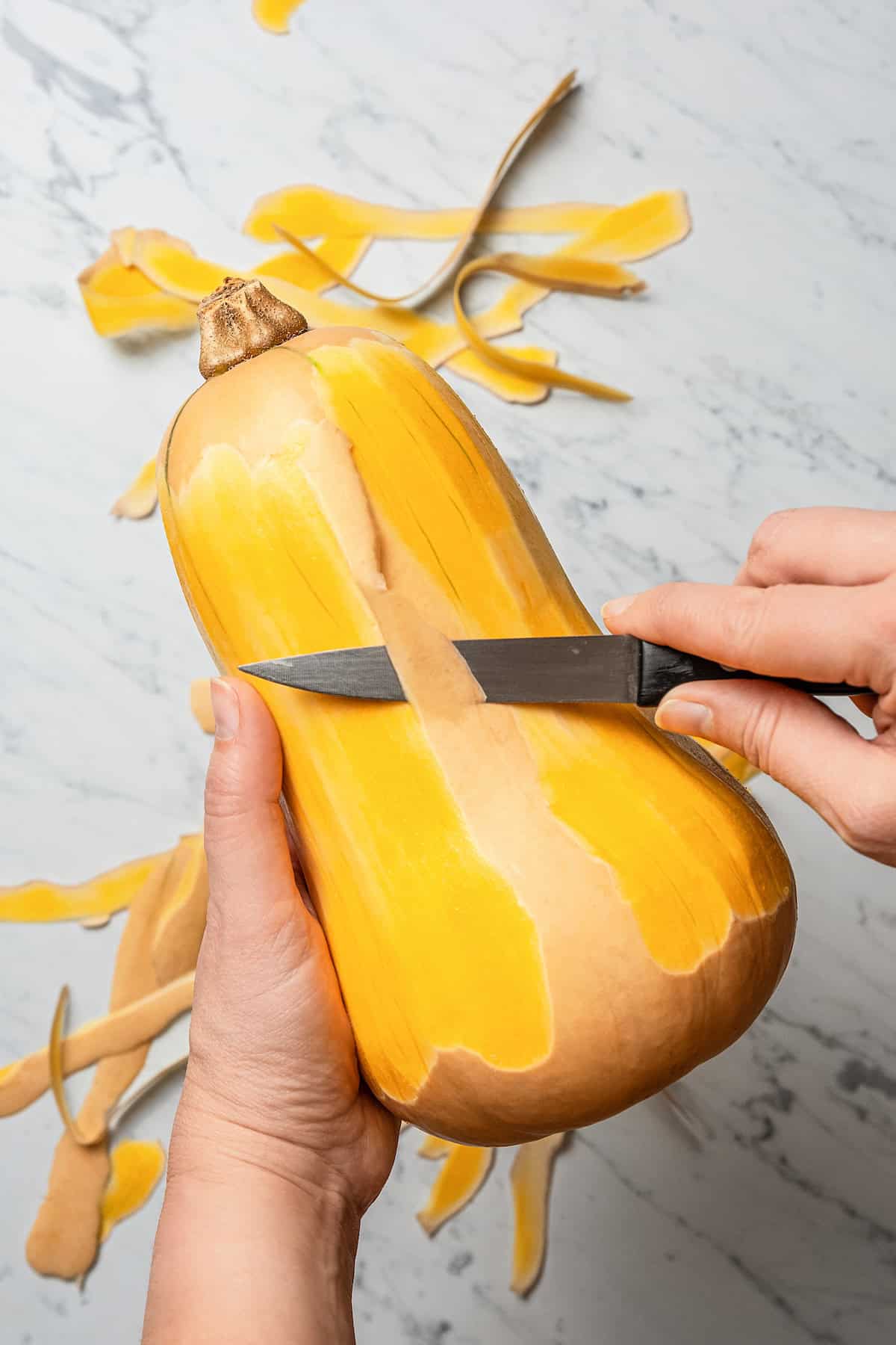 Peeling a butternut squash with a knife.