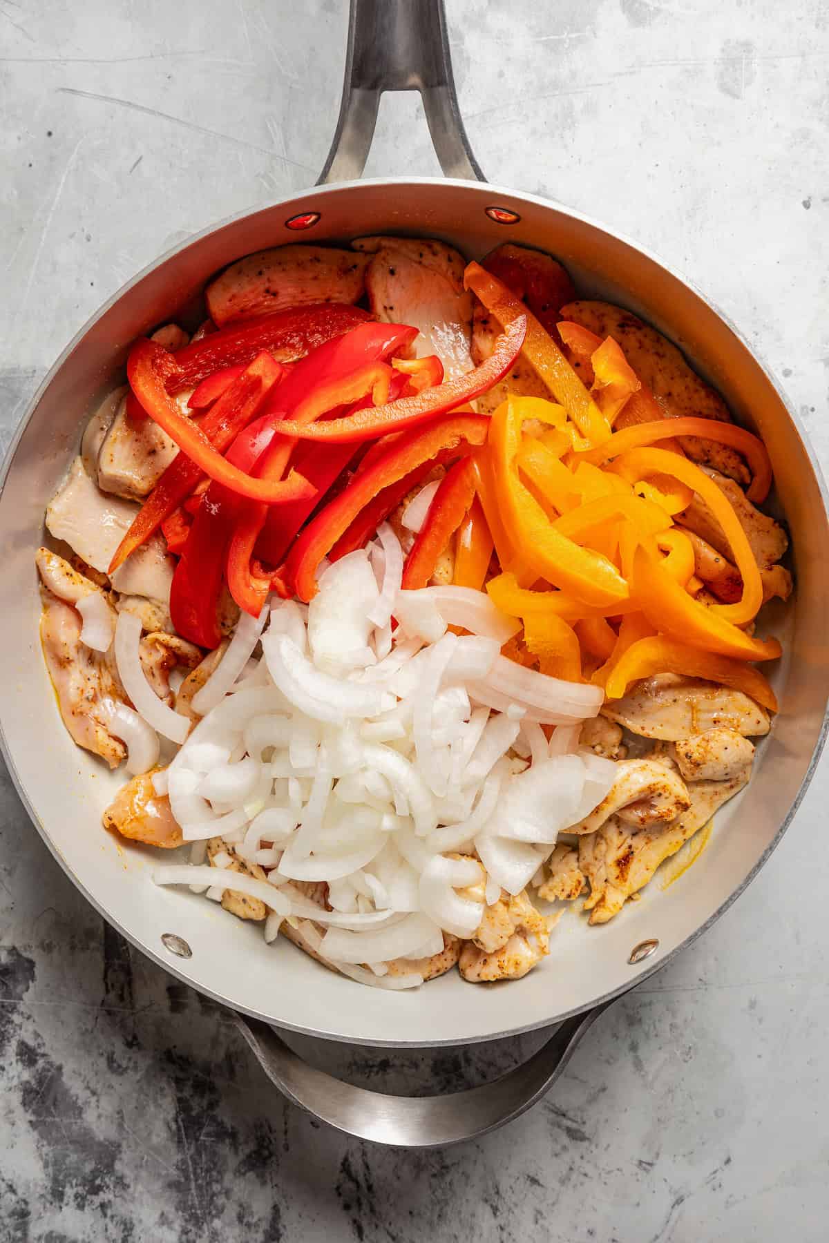 Sliced onions and red and orange bell peppers added to a skillet with cooked chicken.