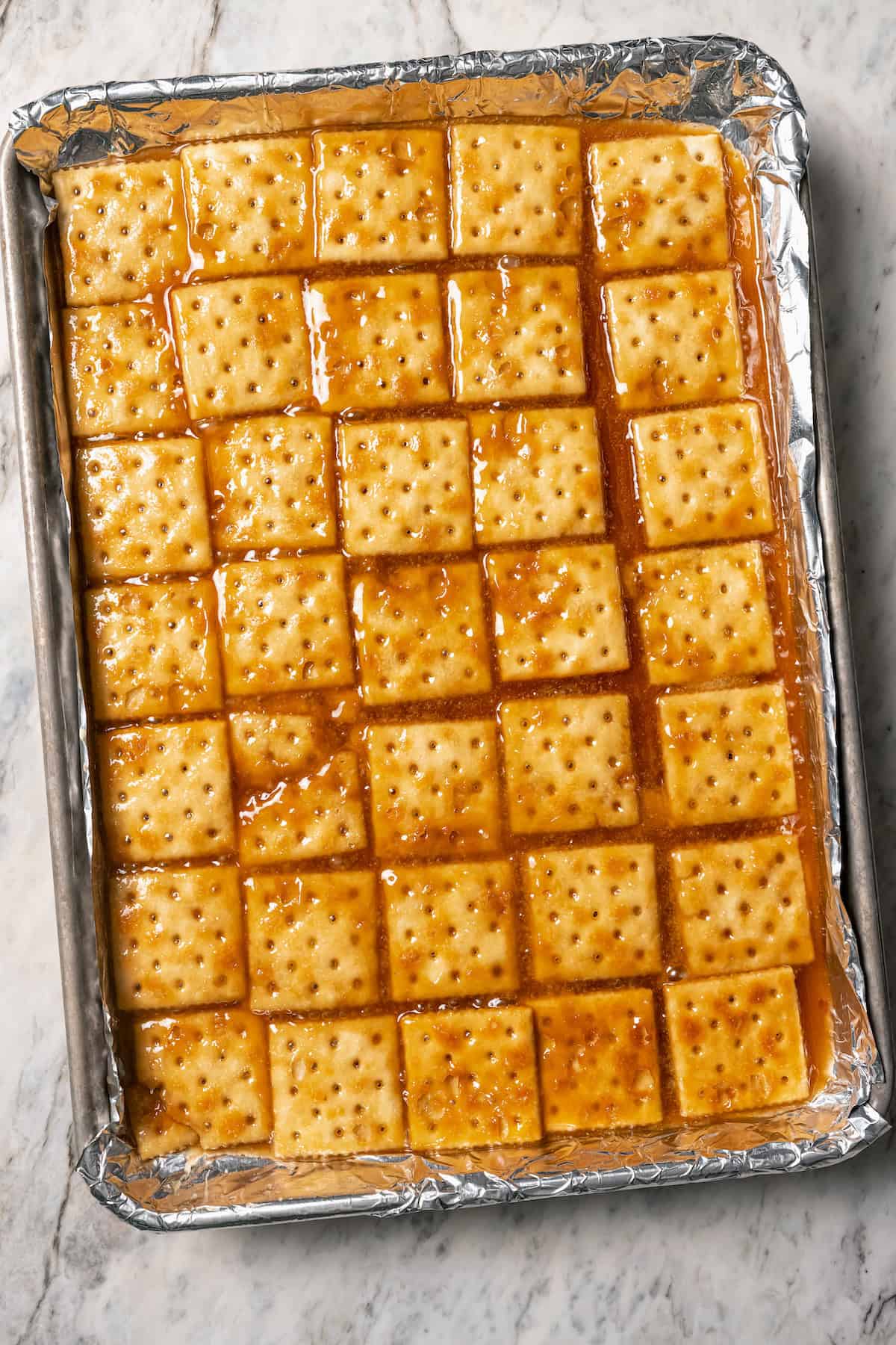 Saltine crackers topped with caramel toffee in a foil-lined sheet pan.