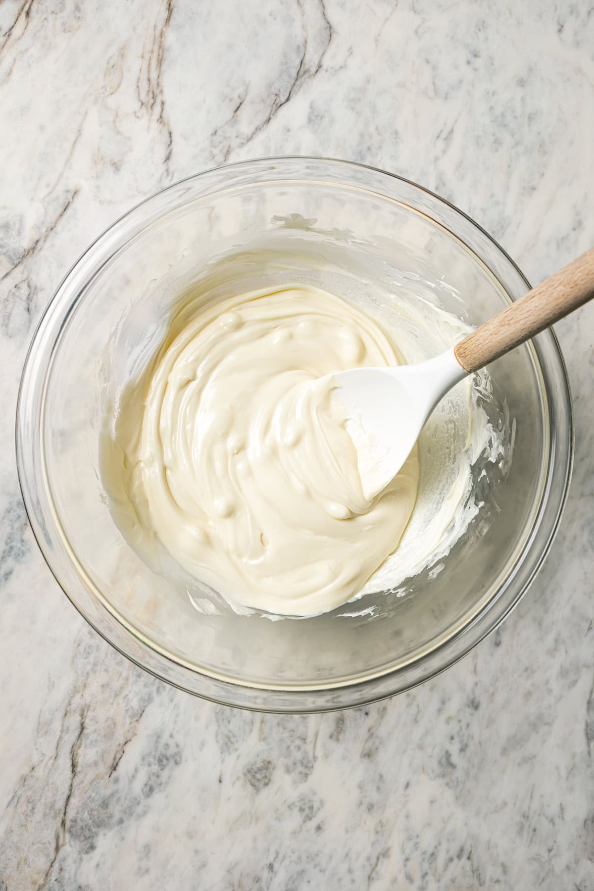 Melted white chocolate in a glass bowl with a spoon.