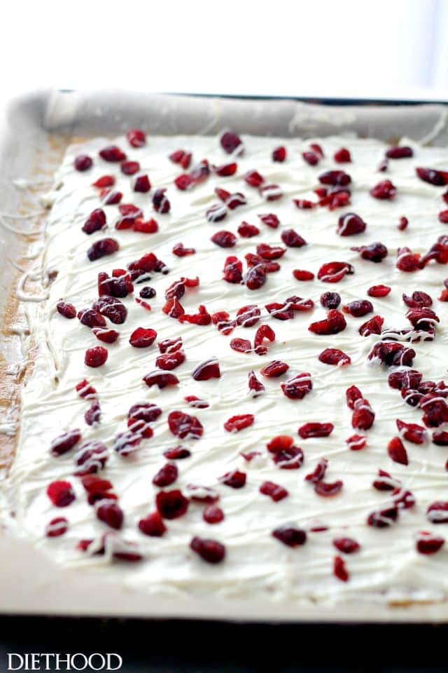Saltine Toffee on a parchment lined baking sheet topped with white chocolate and cranberries