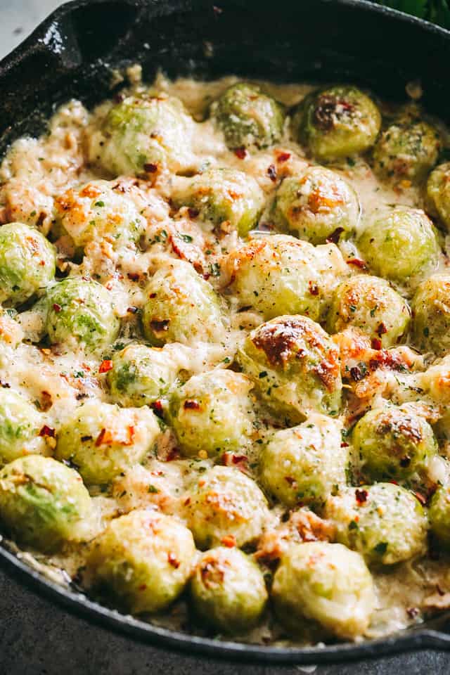 Roasted Brussels sprouts in a skillet covered in a cheesy bacon cream sauce.
